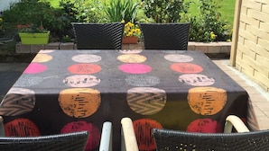 Un área de comedor al aire libre con una mesa cubierta con un mantel estampado, rodeada de sillas de mimbre.