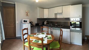 Cocina compacta con armarios blancos, microondas, estufa y lavavajillas. Hay una mesa de comedor con sillas y un mantel individual verde.