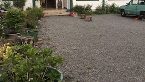 Una casa de dos pisos con techo rojo y detalles verdes, un camino de grava y un coche estacionado.