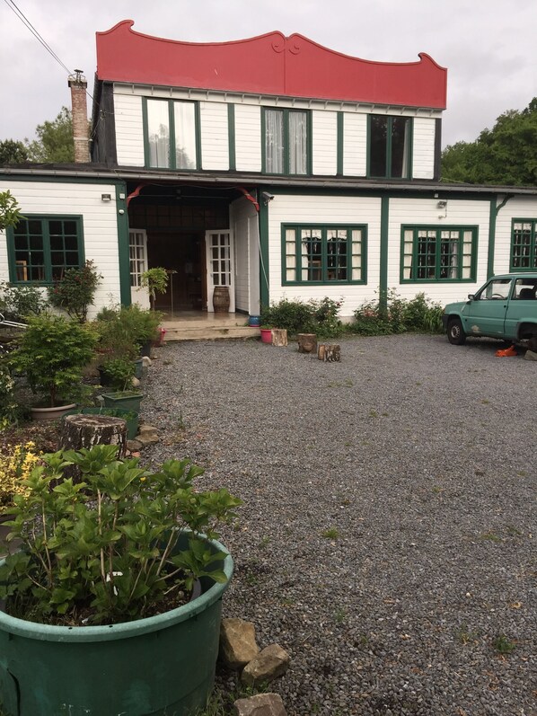 A two-story house with a red roof and green trim, a gravel driveway, and a parked car.
