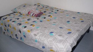 Un lit simple avec une couvre-lit à motifs géométriques et une couverture rose et blanche soigneusement pliée.
