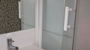 A bathroom with a white sink, a mirror, and a glass shower enclosure. - Lush greenery in the city center (Rouen)