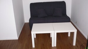 A room with a dark-colored sofa against a white wall, a white table in the center, and wooden flooring. - Lush greenery in the city center (Rouen)