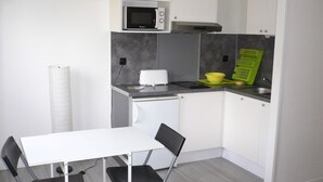 A compact kitchen with a microwave, toaster, and a small sink. There is a white table with two chairs and a roll of paper towels. - Lush greenery in the city center (Rouen)