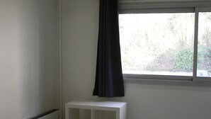 A room with a white console table, a black lamp, and a window with a black curtain. - Lush greenery in the city center (Rouen)