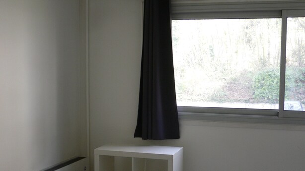 Une pièce avec une console blanche, une lampe noire et une fenêtre ornée d’un rideau noir.