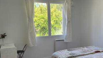 Een slaapkamer met een bed, een bureau en een stoel. Er is een raam met gordijnen, een radiator en een plafondlamp.