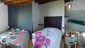 Ein Schlafzimmer mit Bett, Nachttisch und einem kleinen Tisch daneben. Es gibt ein Badezimmer mit Waschbecken, Spiegel und Dusche.