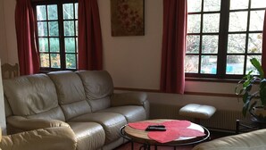 Un salón con un sofá de cuero color crema, una mesita redonda con un posavasos rojo y un radiador.