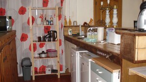 Una cocina compacta con un estante de madera, un refrigerador pequeño y un lavamanos.