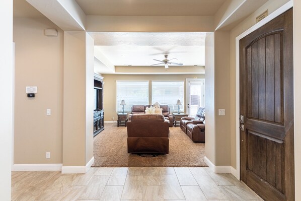 A spacious living room with a brown sectional sofa, a ceiling fan, and a large wooden door.