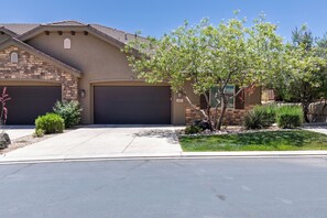 A two-story house with a garage, a well-maintained lawn, and a variety of shrubs and small trees.