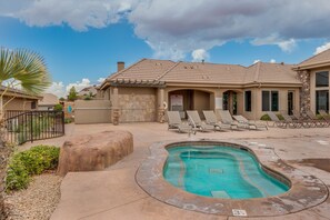 A pool area with a curved pool, lounge chairs, and a stone building with a tiled roof.
