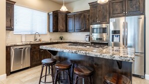 A modern kitchen with dark wooden cabinets, stainless steel appliances, a granite countertop, and bar stools. - Zion's Point-Pet Friendly! (Washington)