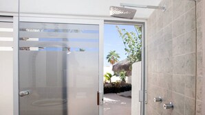 A modern bathroom with a glass door, a shower area, and a view of a tropical outdoor setting. - BEAUTIFUL VILLA WITH PRIVATE POOL (Cabo San Lucas)
