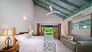 Habitación de hotel con cama, sofá, ventilador de techo y vistas a zonas verdes.
