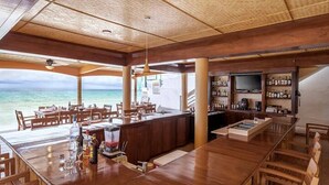 Una zona de bar con mobiliario de madera, un televisor y vistas al océano.