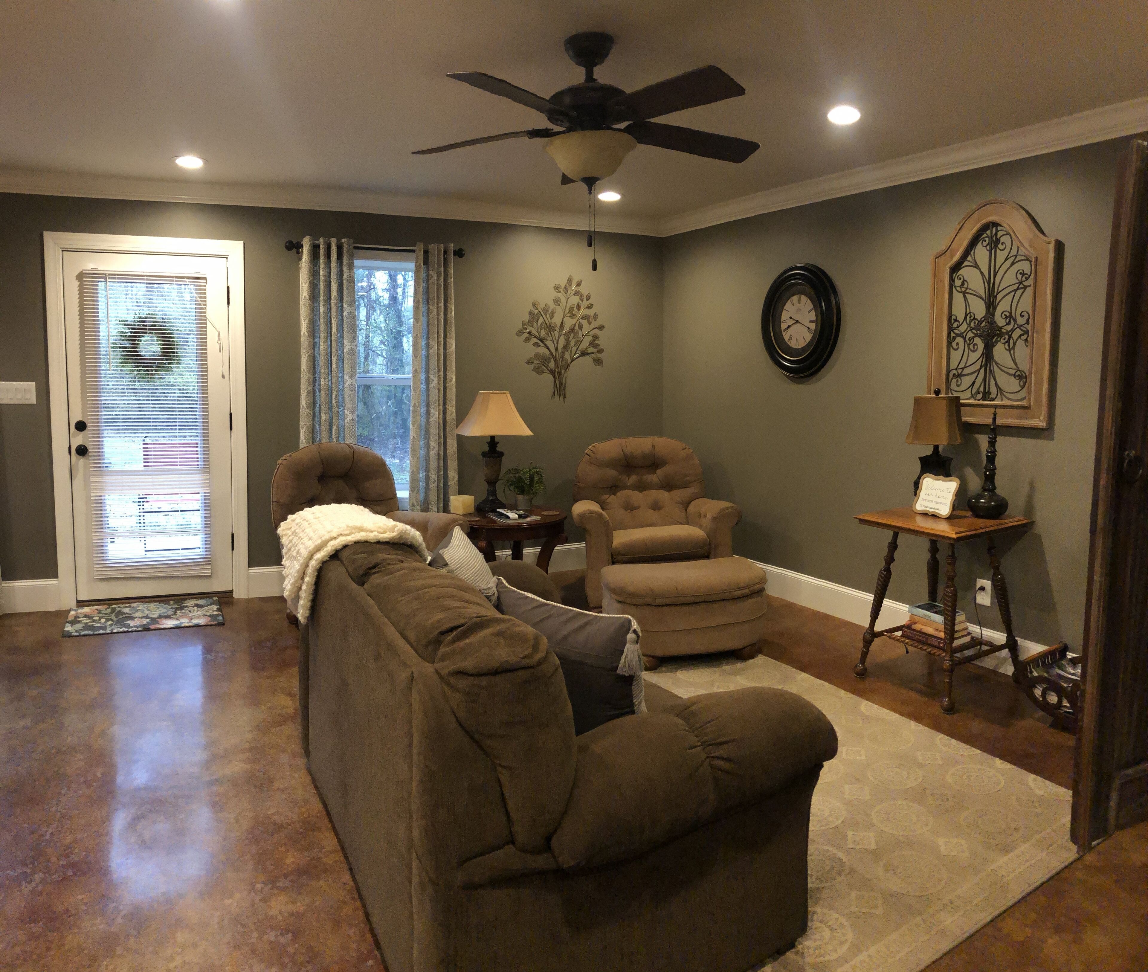 A living room with two brown sofas, a ceiling fan, a clock, and a lamp on a side table.