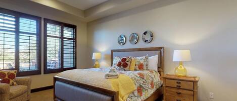 A bedroom with a large bed, two bedside tables, a chair, and three wall clocks.
