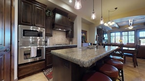 Una cocina moderna con electrodomésticos de acero inoxidable, una isla de granito y un comedor con taburetes de cuero.