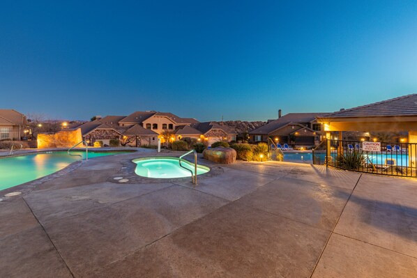 A swimming pool area with a hot tub, lounge chairs, and a caution sign.