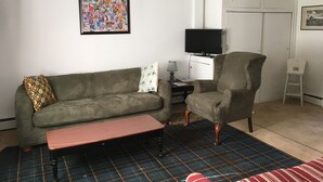 Ein Wohnzimmer mit einer Couch, Sesseln, einer Bank und einem Fernseher auf einem Schrank.