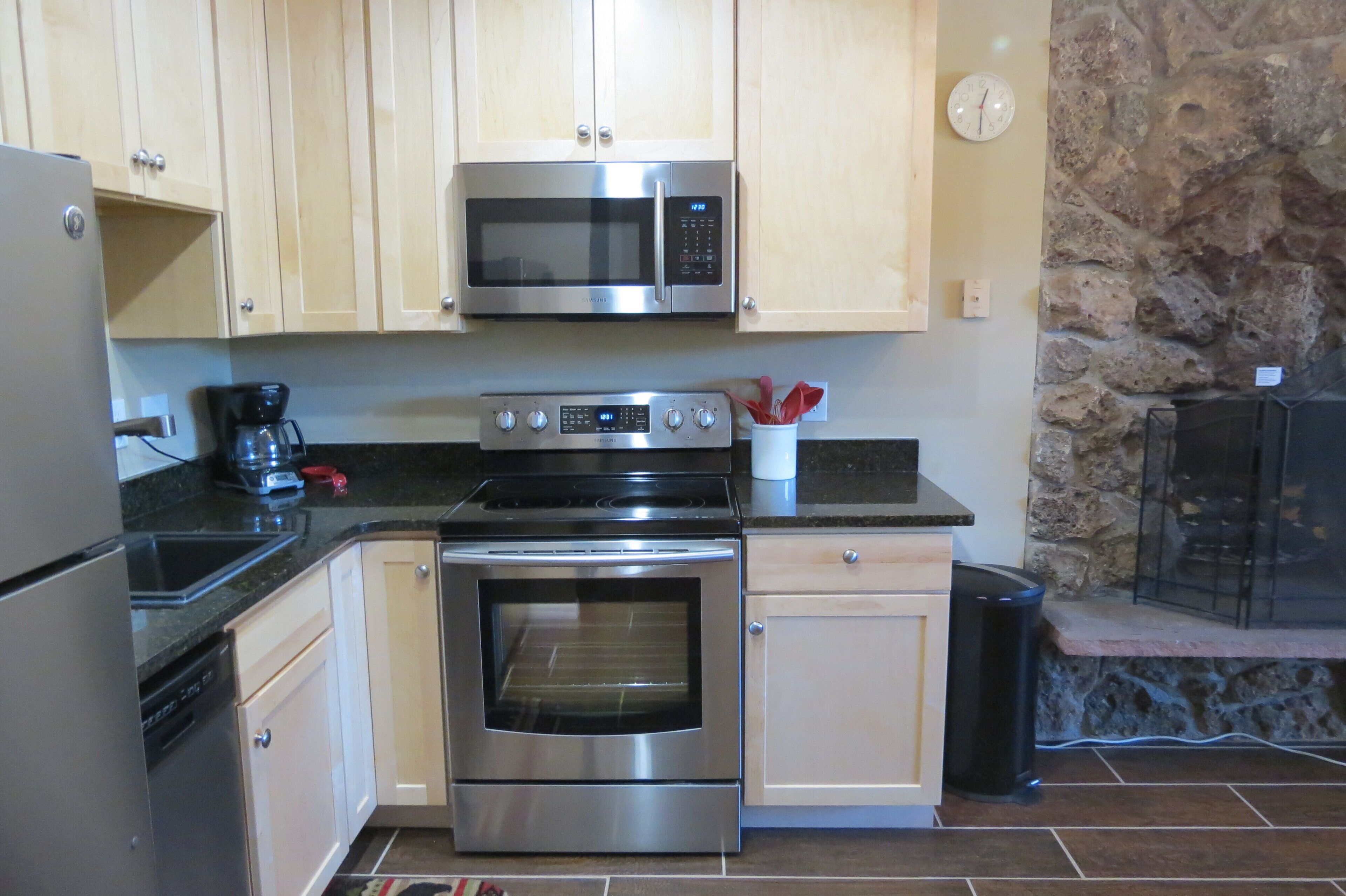 A kitchen with stainless steel appliances, wooden cabinets, a stone wall, and a fireplace.
