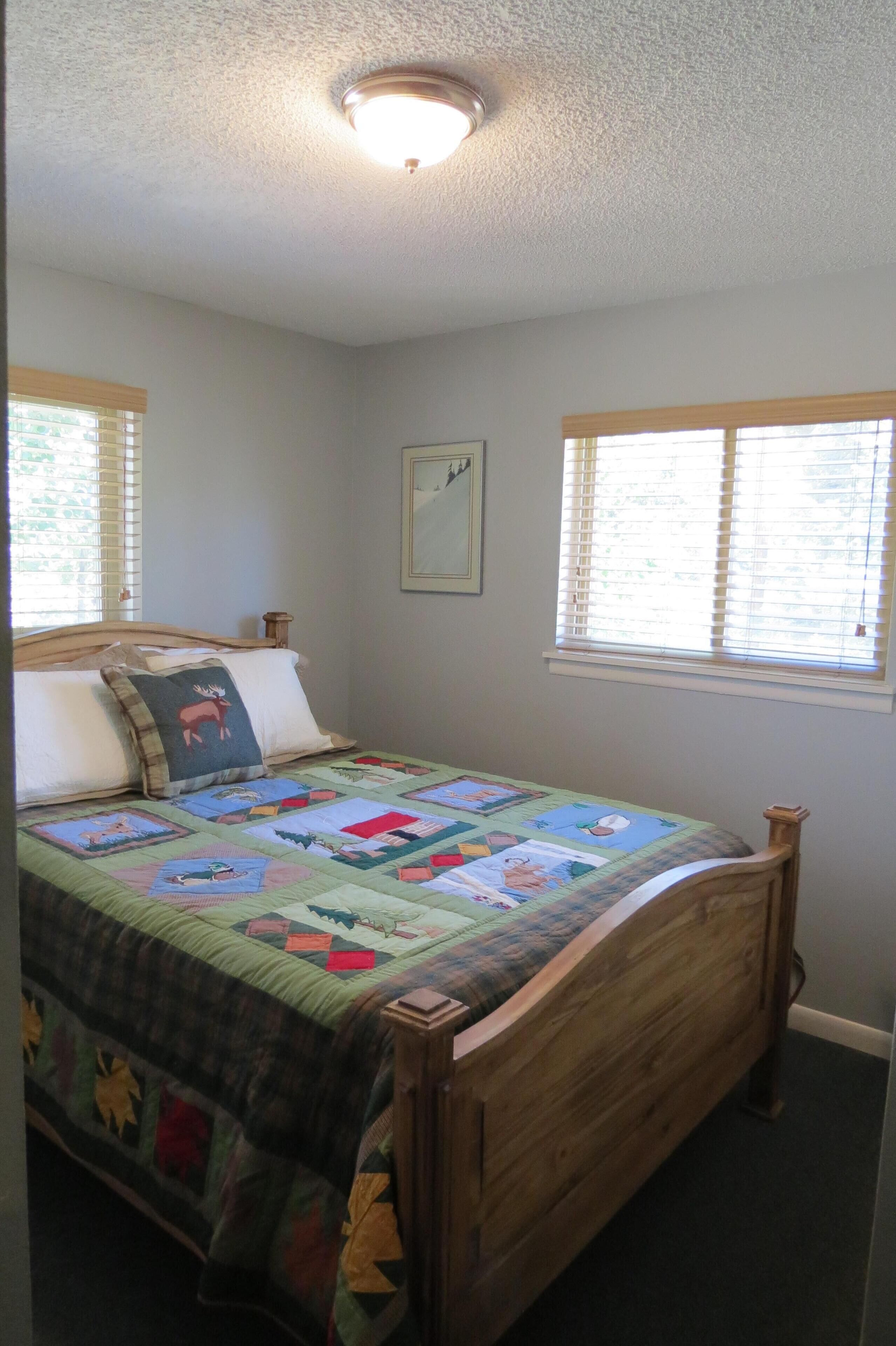 A bedroom with a wooden bed, a quilt, and a window with blinds.