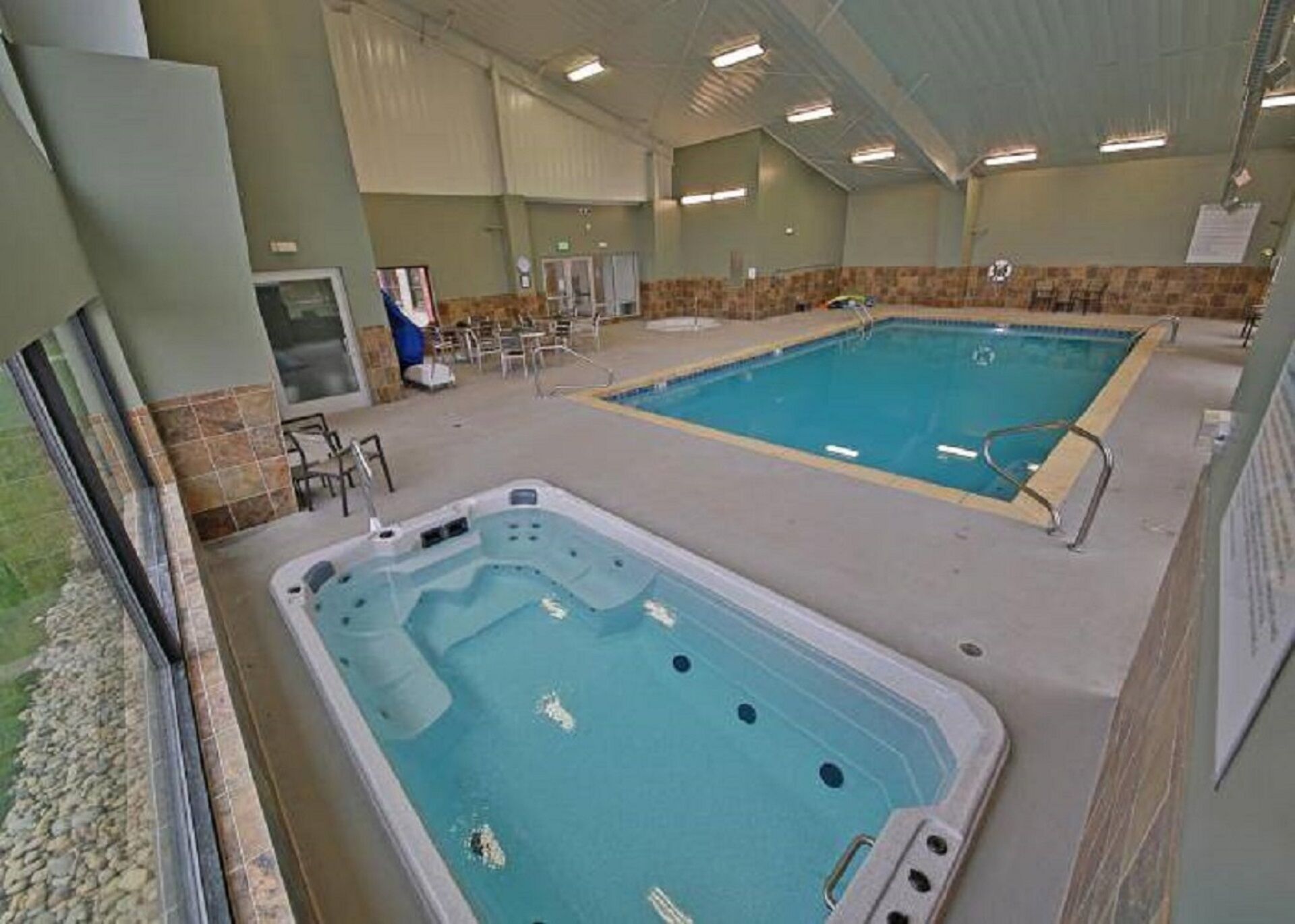 Ein Hallenbad mit Whirlpool und separatem Poolbereich, umgeben von Stühlen und einer gefliesten Wand.