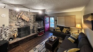 Una sala de estar con pared de piedra, chimenea, sofá y televisor.