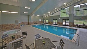 Una piscina interior con suelo de baldosas, rodeada de mesas y sillas de madera.