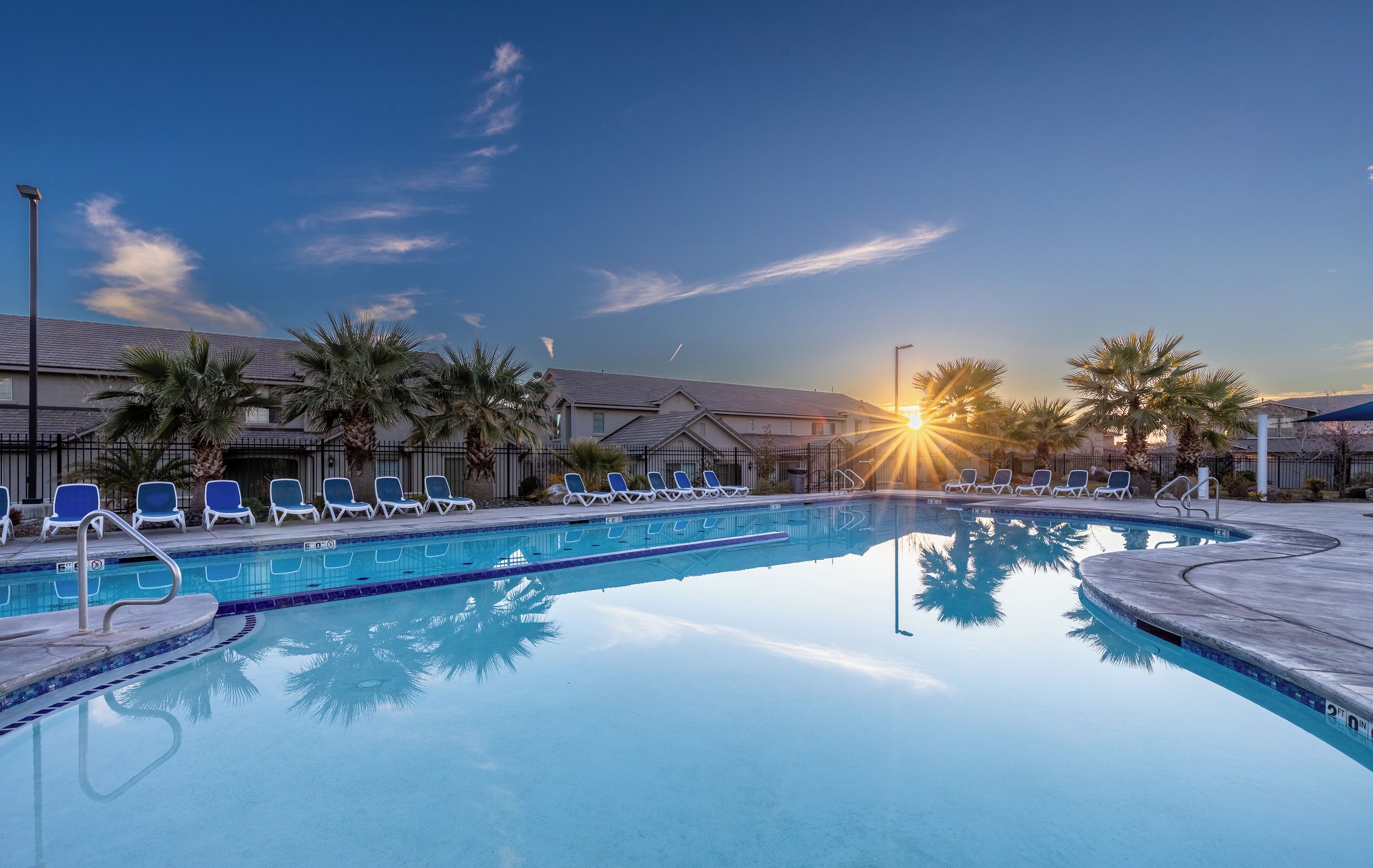 A swimming pool with lounge chairs and palm trees, surrounded by buildings.