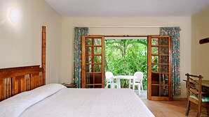 Ein Schlafzimmer mit einem Bett, einem Holzkopfbrett, einem Schreibtisch mit Stuhl und Blick auf einen Garten durch eine offene Tür.