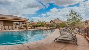 A pool area with lounge chairs, a covered seating area, and a view of residential buildings.