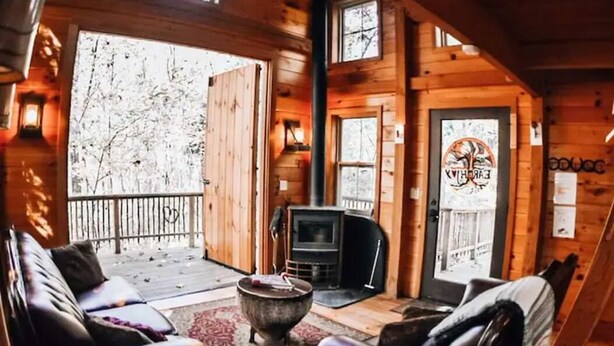 A cozy cabin interior with a fireplace, wooden walls, and a balcony with a view of trees. - Stay in Tree House built by TreeHouse Master Pete Nelson ~ off the grid (Germantown)