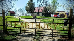 A rural landscape with a wooden gate labeled "EARTHJOY" leading to a dirt path. - Stay in Tree House built by TreeHouse Master Pete Nelson ~ off the grid (Germantown)