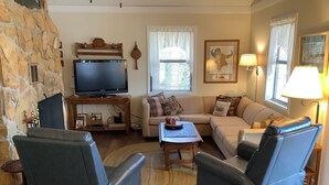 Un salon avec un mur en pierre, un téléviseur, un canapé, deux fauteuils, une table basse et une lampe.