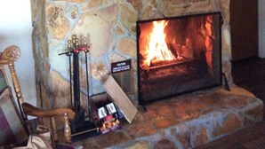 Une cheminée en pierre avec un feu de bois, une chaise en bois et une petite table sur laquelle sont posés divers objets.