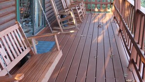 Une terrasse en bois avec des chaises et un banc, une porte vitrée et une vue sur les arbres.