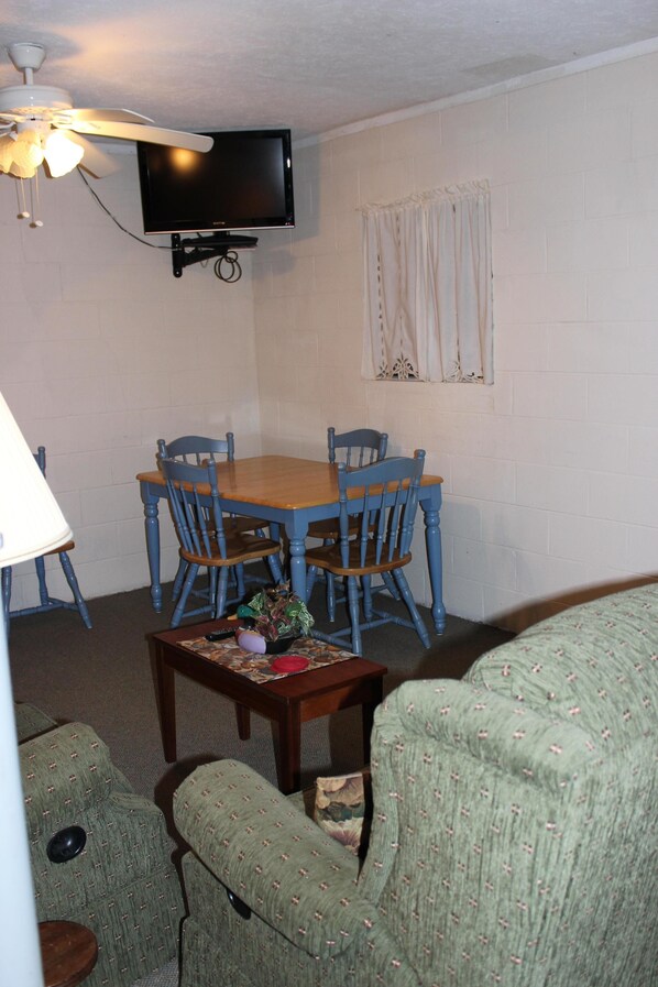 A dining area with a wooden table and blue chairs, a television mounted on the wall, and a window with curtains. - CABIN FEVER ON LAKE NOTTLEY WITH DOCK (Blairsville)