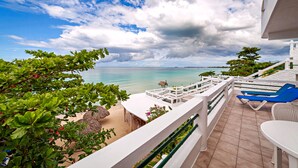 A balcony with a view of the sea, a white railing, and a table with a chair. - Beach House Condos: Beachfront Penthouse - 7mile Beach Jamaica (Negril)