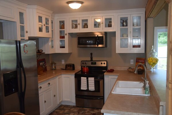 A kitchen with white cabinets, a stainless steel refrigerator, a microwave, a stove, and a sink. - The Barn in Hendersonville (Hendersonville)