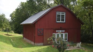 Ein rotes Bauernhaus mit Satteldach, einem großen Fenster und einer Tür.
