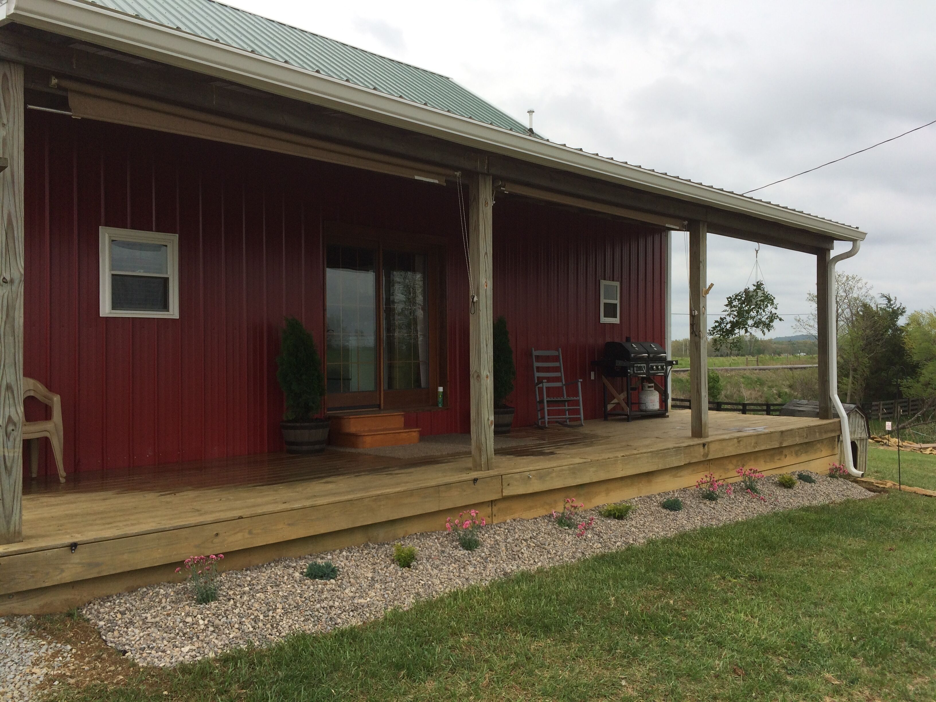 A red barn with a covered porch, a small window, and a grill on the porch.
