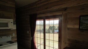 Een blokhut interieur met houten wanden, een schuifglazen deur naar een tuin, een magnetron en een fornuis.