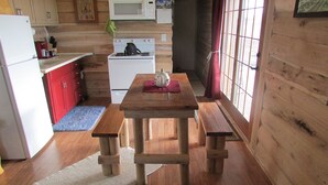 Een knus, compact keuken met houten wanden, een houten tafel met bankjes, een magnetron, een fornuis en een koelkast.