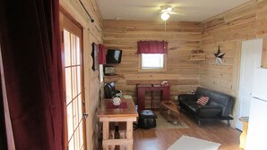 Een gezellig interieur van een chalet met houten wanden, een plafondventilator, een houten tafel, een leren bank en een aan de muur bevestigde televisie.