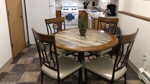 Une cuisine avec des meubles en bois, un réfrigérateur blanc, une cuisinière et un évier. On y trouve une table ronde avec des chaises et une plante en pot.