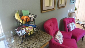 Una encimera de cocina con una cesta de frutas, una silla y una lámpara.