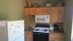 Una cocina con armarios de madera, un refrigerador blanco, un microondas, una estufa y una cafetera.